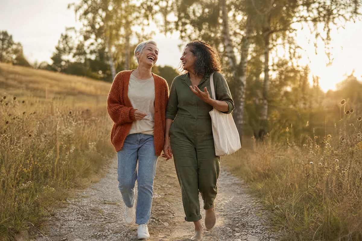 Zwei Freundinnen gehen lachend einen Wiesenweg entlang
